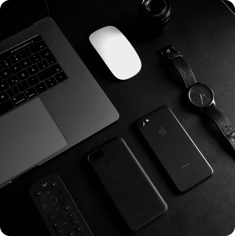 Macbook posé sur une table avec un Iphone, une coque de smartphone, une montre ainsi qu'une télécommande Xbox à côté